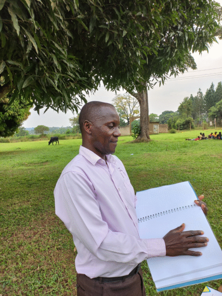Paul aus Uganda liest draussen im Grünen aus der Braillebibel